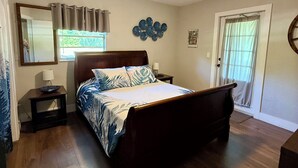 A bedroom with a bed, a ceiling fan, a nightstand, a window with curtains, and a door.