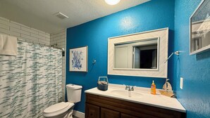 A bathroom with a blue wall, white toilet, and wooden vanity with a mirror.