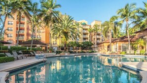 Ein Hotelpool mit Palmen und einem Gebäude mit Balkonen im Hintergrund.