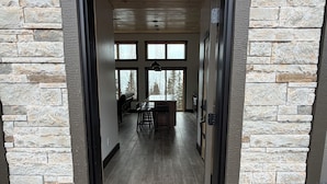 A stone-framed doorway leading into a room with a long view through large windows, a central light fixture, and a bench.
