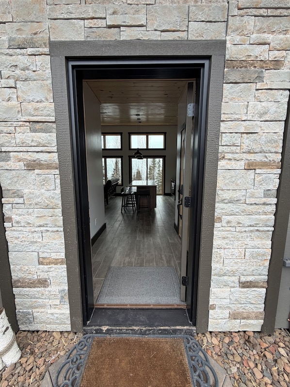 A stone-framed doorway leading into a room with a long view through large windows, a central light fixture, and a bench.