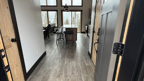 A hallway leading to a dining area with a wooden ceiling, large windows, and a central island with stools.