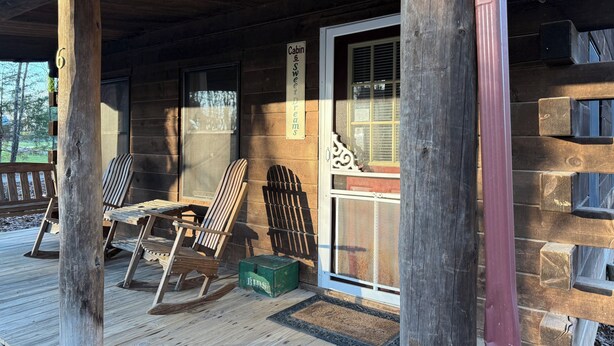 A wooden cabin with a porch, rocking chairs, a green box, and a sign reading 'Cabin Sweet Dreams.'