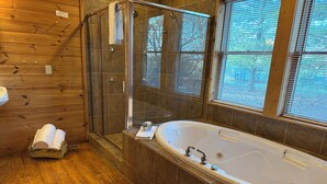 A bathroom with a glass-enclosed shower, a freestanding bathtub, and a window with blinds.