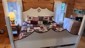 Ein Schlafzimmer in einer Holzhütte mit einem Bett, einem Nachttisch, einer Lampe und einem Fenster.