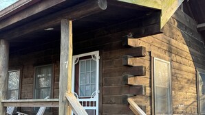 Eine Holzhütte mit Veranda, einer Tür mit einer Nummer und Fenstern.