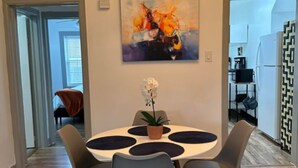 Un coin repas avec une table ronde, quatre chaises, une plante en pot et un tableau accroché au mur.