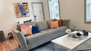 Un salon avec un canapé gris, des coussins colorés, une table basse et une œuvre d’art murale.