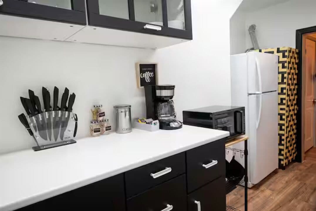 A kitchen with a coffee machine, microwave, refrigerator, and black cabinets.