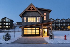 A multi-story residential building with a garage, stone facade, and a clear view of the surrounding area. - New Luxury Mountain Home | Hot Tub | 3 Fireplaces (Winter Park)