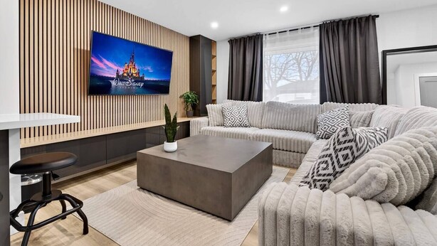Ett modernt vardagsrum med en platt-TV, en soffgrupp, ett soffbord och en barhörna.