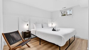 Ett modernt hotellrum med en säng, sängbord, en stol och ett fönster.