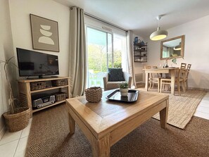 A living room with a TV, wooden coffee table, and a dining area with a table and chairs. - Fouesnant Beg Meil, 100m from the beach, beautiful apartment with swimming pool (BEGMEIL)
