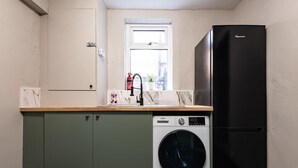 A compact kitchen with a washing machine, a black refrigerator, and a window above the sink. - Ebe Lively Newland Ave 4 BR 5 TVS 1.5 Bath House (Kingston upon Hull)