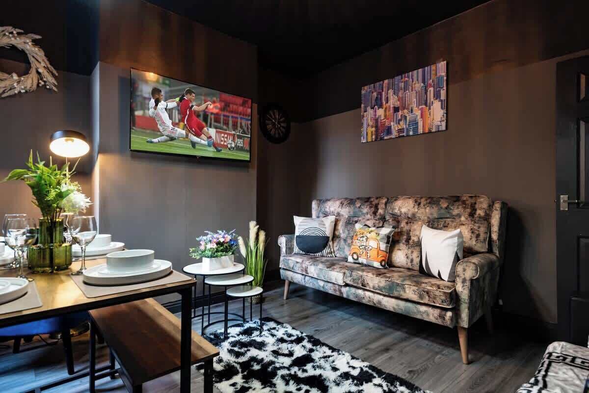 Ett modernt vardagsrum med en soffa, ett matbord dukat med tallrikar och glas, en tv och en tavla som föreställer en stadsbild.