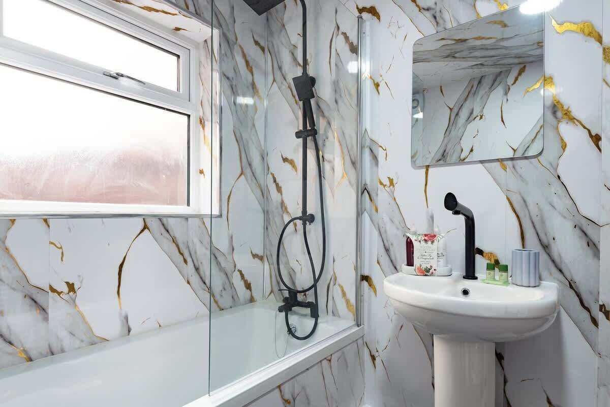 A bathroom with a glass-enclosed shower, a white sink, and a marble-patterned wall.