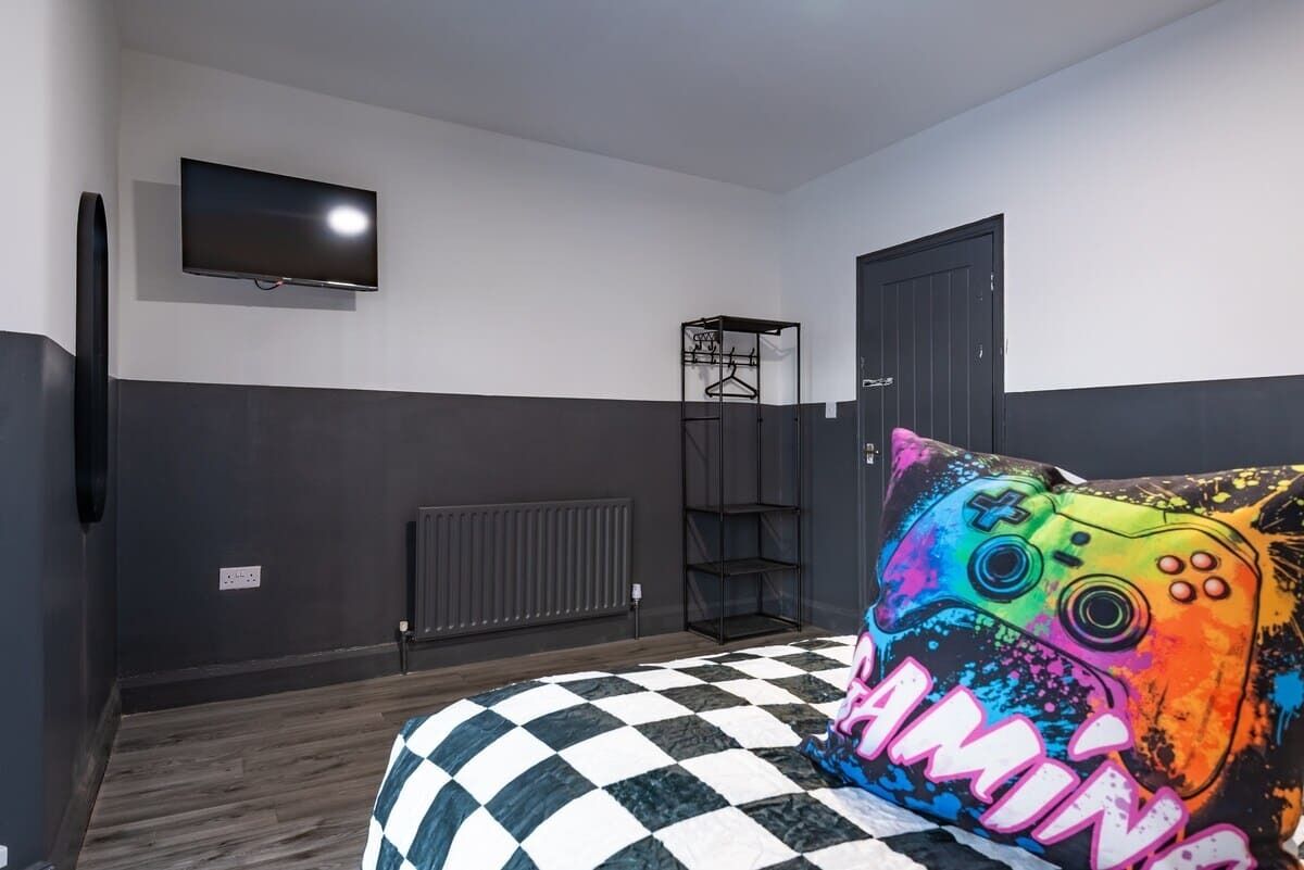 Un dormitorio con edredón a cuadros, televisor montado en la pared, radiador y una puerta.