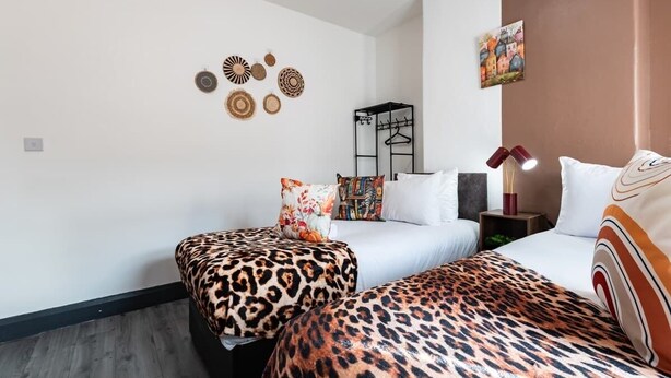 A hotel room with two beds, each with a leopard print bedspread, white bedding, and a variety of decorative items on the walls. - Ebe Lively Newland Ave 4 BR 5 TVS 1.5 Bath House (Kingston upon Hull)
