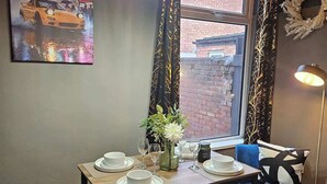 A dining area with a table set for four, a bench, a vase with flowers, and a painting of a car on the wall. - Ebe Lively Newland Ave 4 BR 5 TVS 1.5 Bath House (Kingston upon Hull)