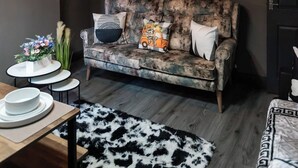 A cozy living room with a sofa, a flat-screen TV, a clock, and a cityscape painting. - Ebe Lively Newland Ave 4 BR 5 TVS 1.5 Bath House (Kingston upon Hull)