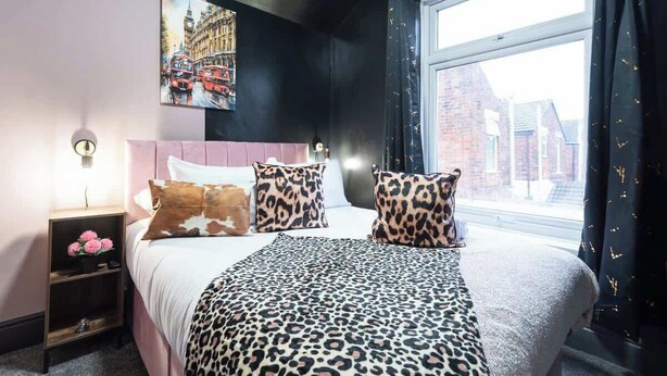 Een slaapkamer met een bed, nachtkastje, lamp en een raam met gordijnen.