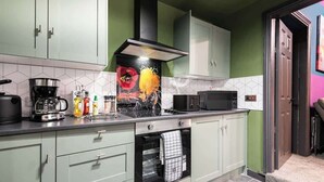 Een keuken met lichtgroene kastjes, een zwarte afzuigkap, een magnetron en een koffiezetapparaat op het aanrecht.