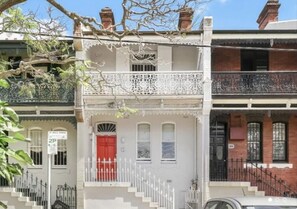 Ein zweigeschossiges Gebäude mit roter Tür, weißen Geländern und einem Balkon mit aufwendiger Gestaltung.