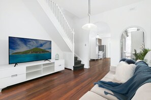 Ein modernes Wohnzimmer mit Fernseher, Holzboden, einer Treppe und einer gemütlichen Sitzecke.