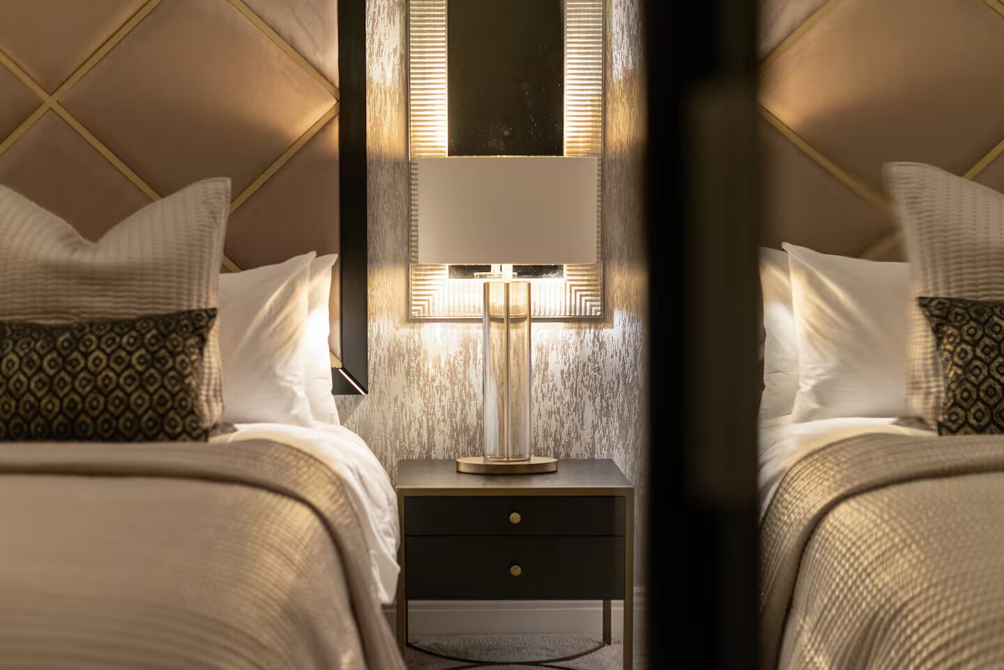 Een hotelkamer met twee bedden, een nachtkastje met een lamp en een spiegel.