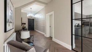 Ein modernes Interieur mit einer Couch, einer Lampe, einem Essbereich und einer durch Glastüren einsehbarer Küche.