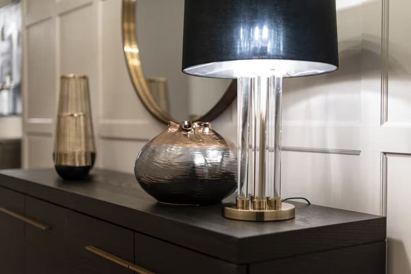 A modern lamp with a cylindrical base and a black shade, placed on a dark wooden dresser.