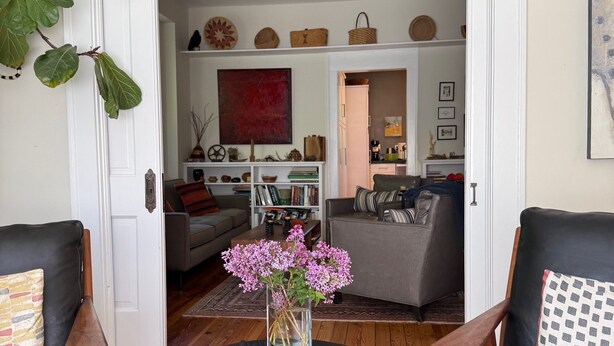 Olohuoneessa on musta pöytä, kaksi nahkaista nojatuolia, maljakko, jossa on kukkia, ja näkymä ruokailutilaan.