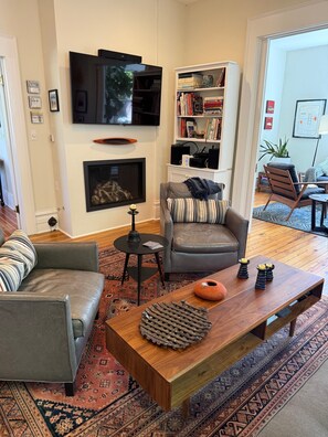 Ein Wohnzimmer mit Kamin, Fernseher, Bücherregal und einer Couch.