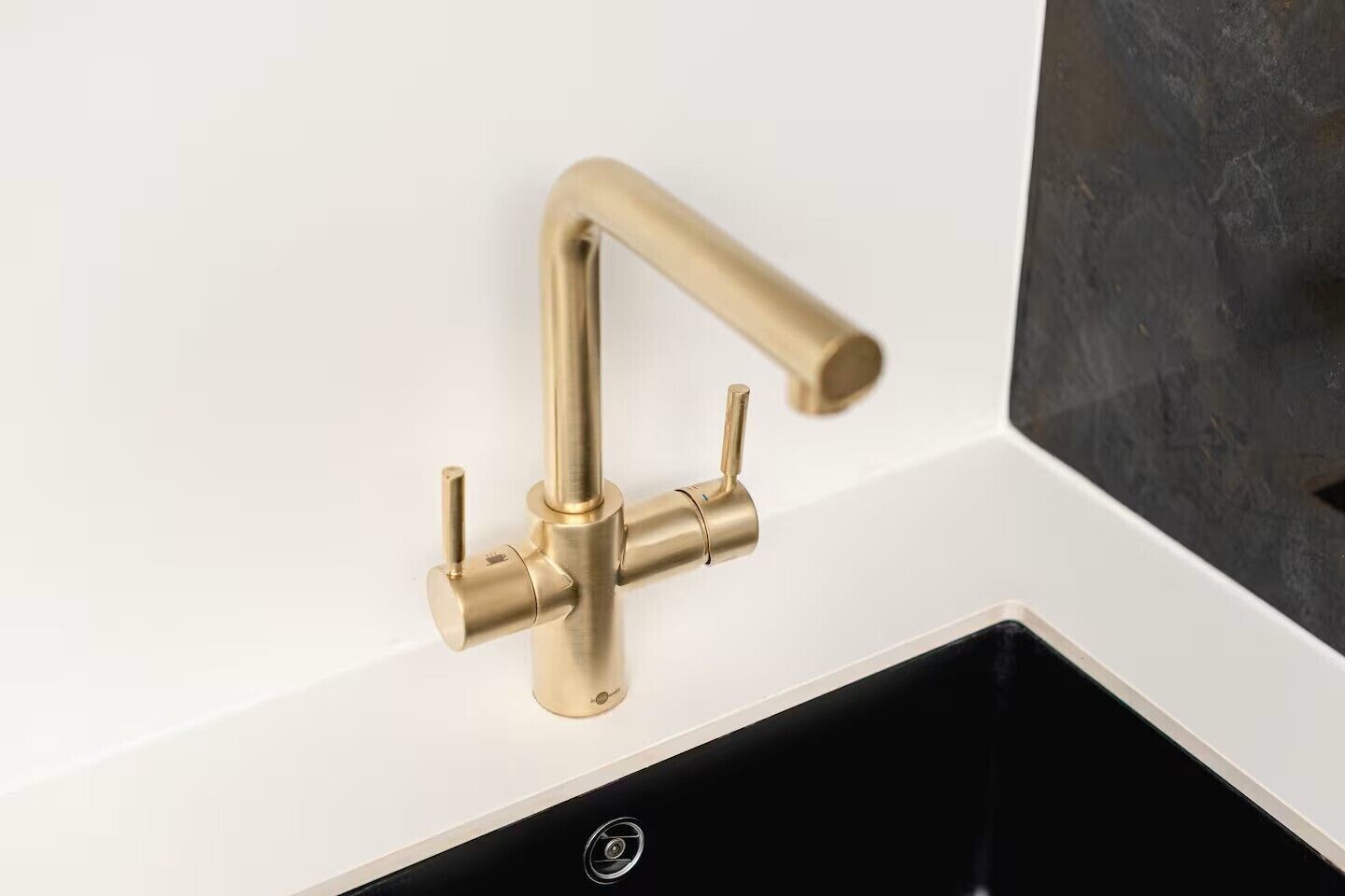Una cocina moderna con grifo dorado, encimera blanca y pileta negra.