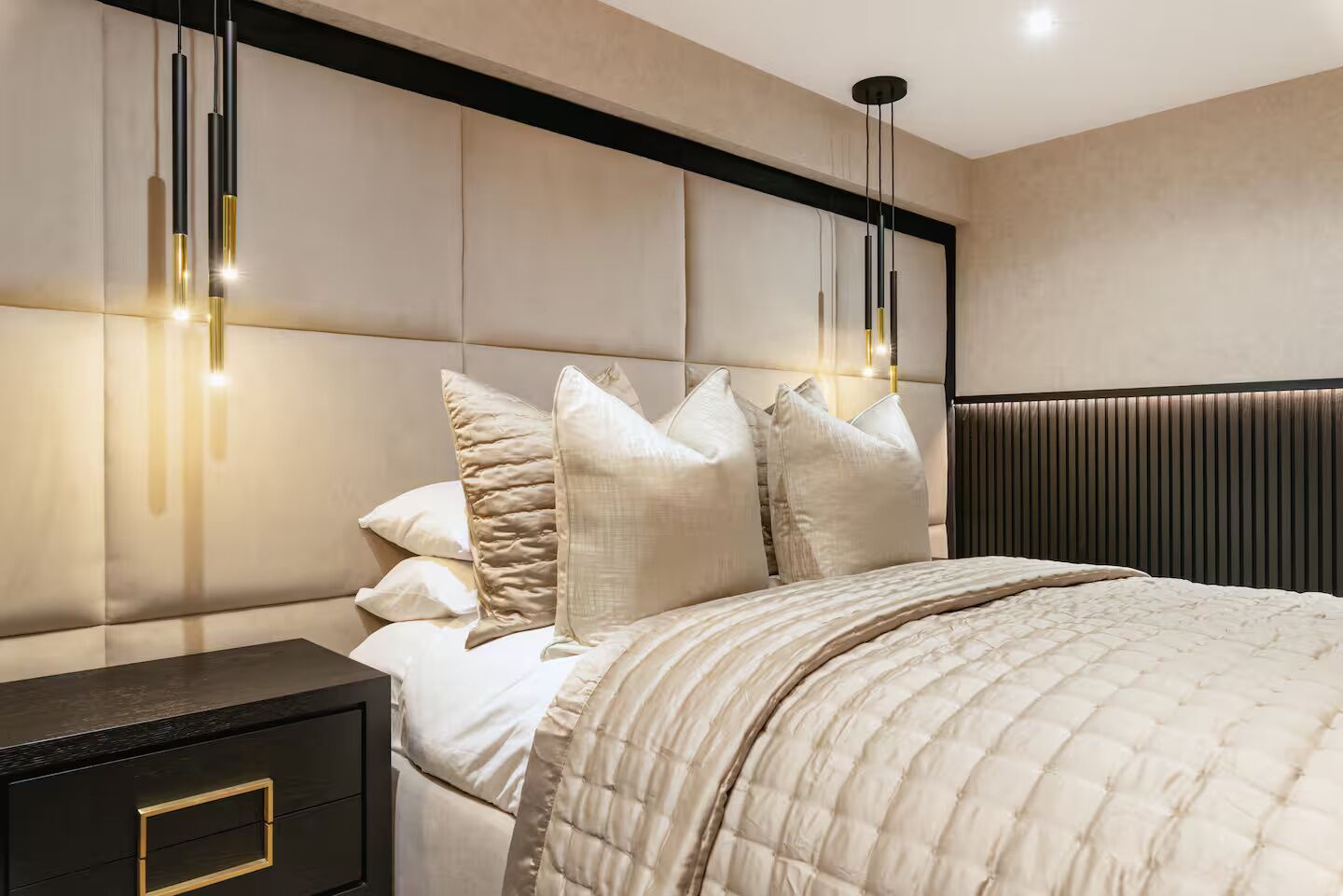 A modern bedroom with a bed, bedside tables, and a headboard with built-in lighting.
