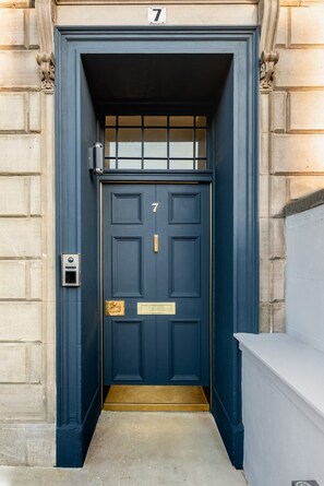 A dark blue door with the number 7, a small mailbox, and a white bench to the right. - Luxury City Centre Apartments  (Edinburgh)