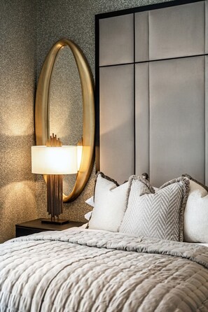 Una cama con un edredón acolchado, una lámpara de noche, un espejo grande y un cabecero con diseño de panel.