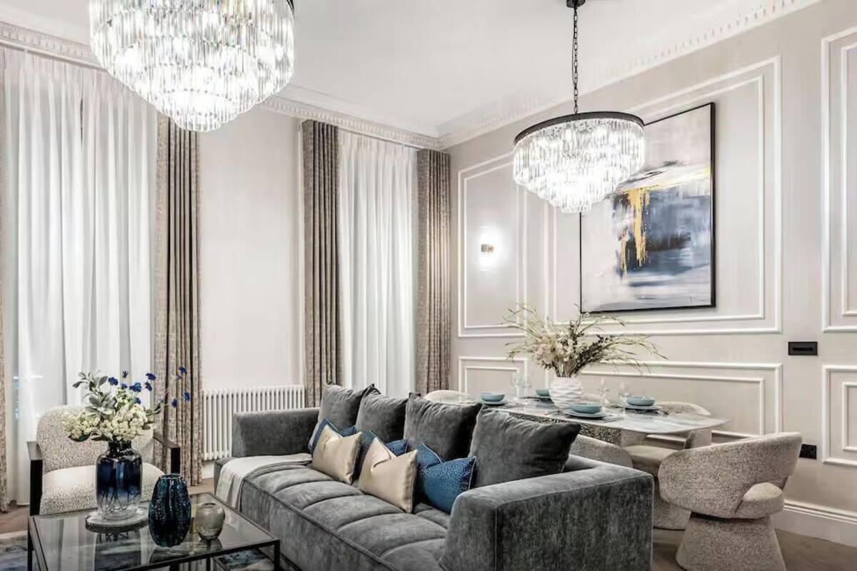 A modern living room with a grey sofa, a glass coffee table, and a chandelier.