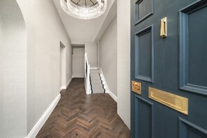 A hallway with a wooden herringbone floor, a blue door with gold handles, and a staircase with white railings. - Luxury City Centre Apartments  (Edinburgh)