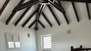 Una sala de estar con un sofá modular, una mesa de centro de vidrio, una ventana con persianas, una puerta y un techo de madera.