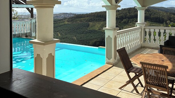 Zona de piscina con vistas a un paisaje montañoso, una mesa con sillas y una estructura de pérgola.