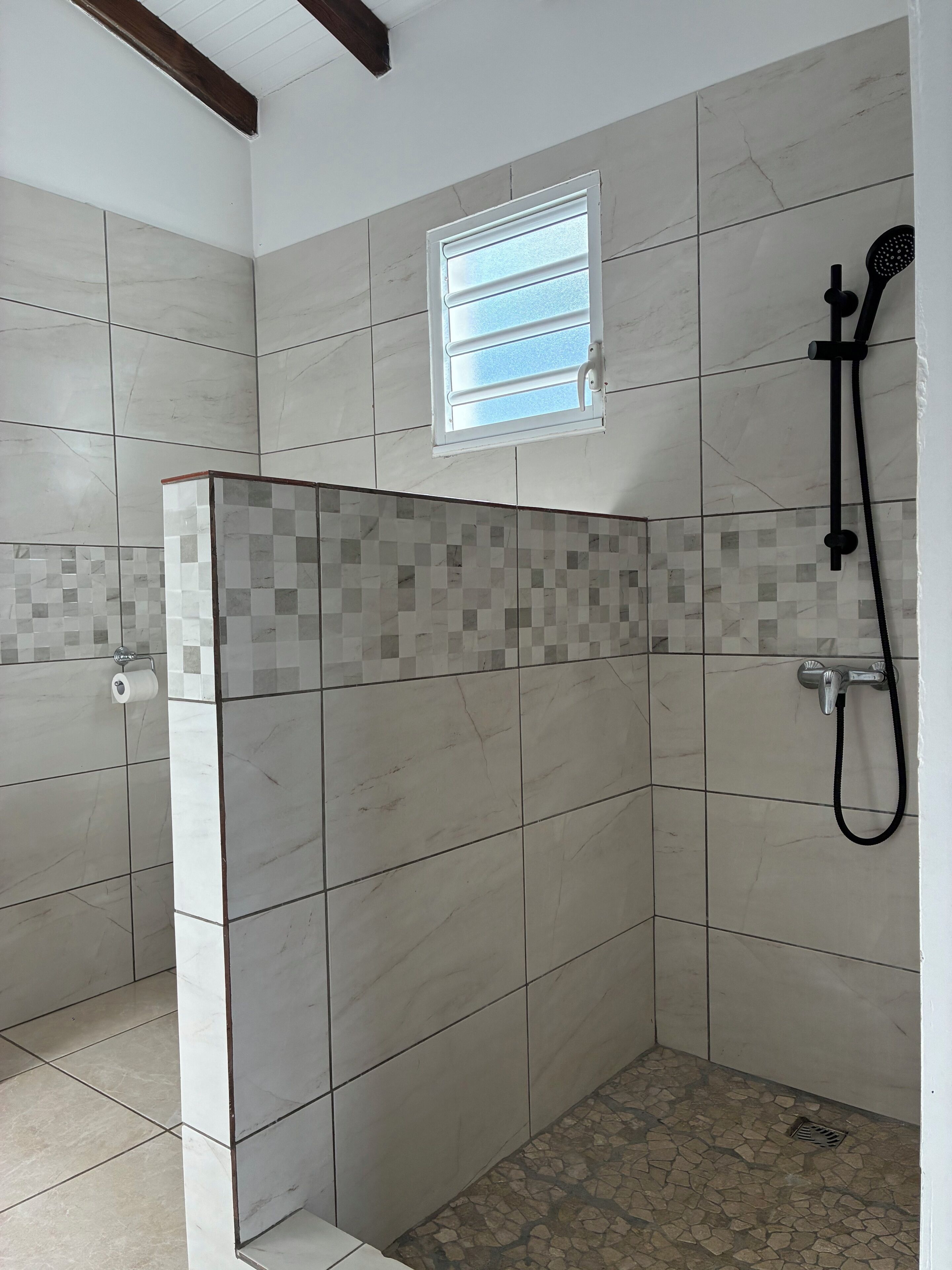 Un área de ducha con paredes de azulejos, una ventana y un cabezal de ducha manual.