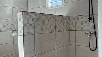 Un área de ducha con paredes de azulejos, una ventana y un cabezal de ducha manual.