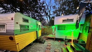 Un camping con dos vehículos recreativos, una terraza de madera y un baño químico.