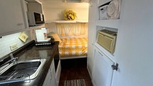 Una kitchenette compacta con microondas, pileta y un pequeño comedor con una cama.