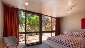 A bedroom with a bed, a chair, and large windows.