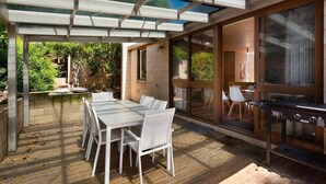 An outdoor patio with a table and chairs, a grill, and a view of greenery.