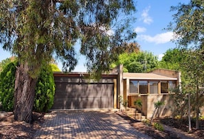 A modern house with a brick driveway, a garage, and a small garden area. - Retro Reservoir Retreat (Strathdale)