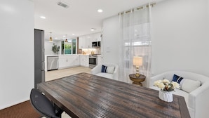 A modern kitchen with white cabinets, a dining area with a wooden table, and a white sofa with a vase of flowers. - Casa Esmeralda -Heated Pool, Luxury BBQ & Patio (Houston)