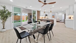 A modern kitchen with a central island, a dining area with a glass table, and a ceiling fan. - Casa Esmeralda -Heated Pool, Luxury BBQ & Patio (Houston)